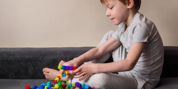 Menino brincando com brinquedos de montar coloridos em um sofá, demonstra criatividade e diversão ao montar peças de plástico, em ambiente interno.