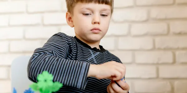 Criança brincando com peças de montagem coloridas em um ambiente interno, focada na atividade e no jogo criativo